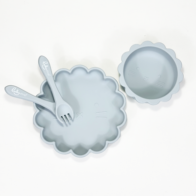 Sky blue sunshine-shaped silicone baby feeding set photographed from top view, showing plate, bowl, fork and spoon